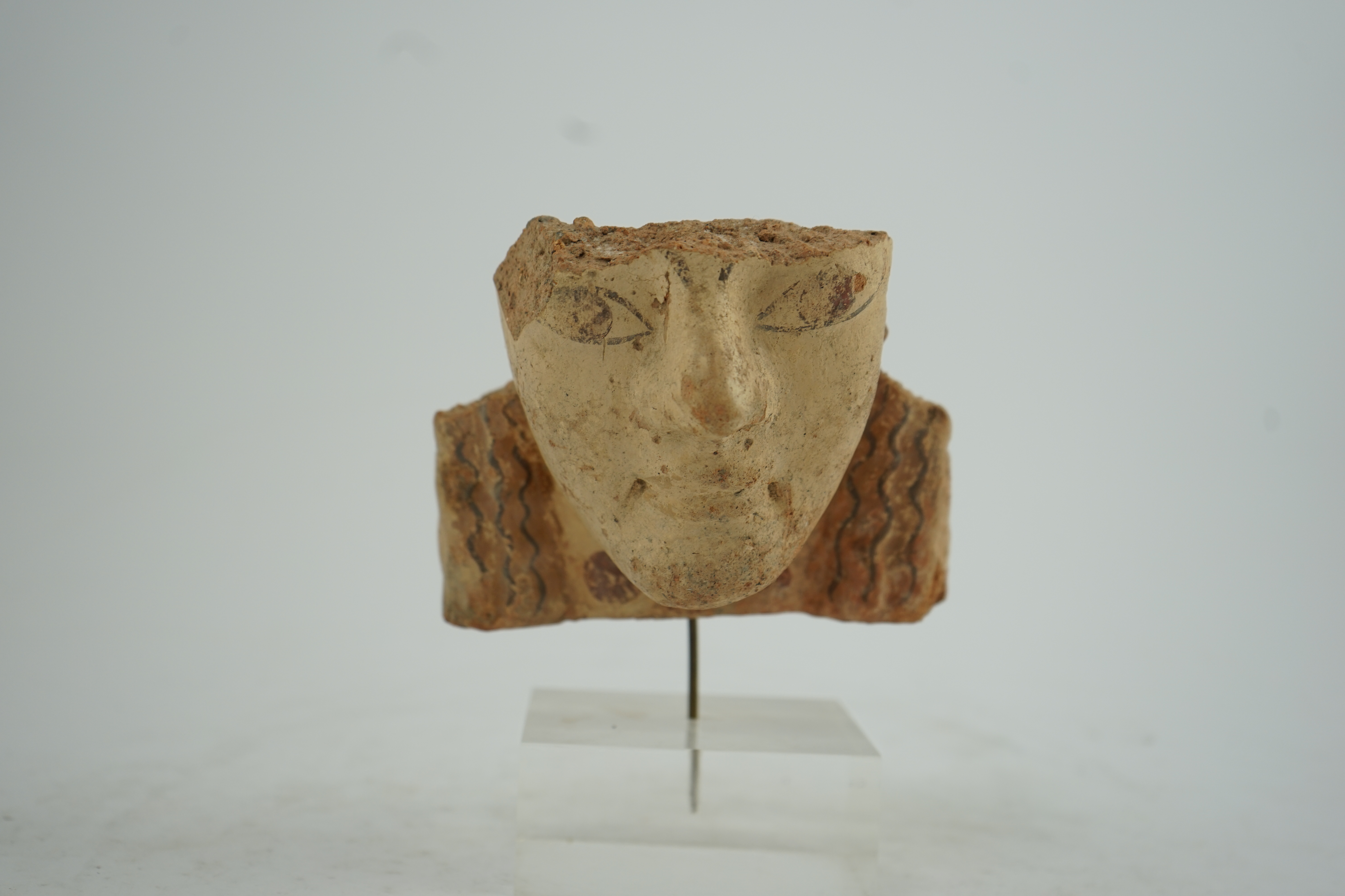 An Etruscan terracotta antefix, modelled as a head with polychrome painted features, 6th-5th century BC.